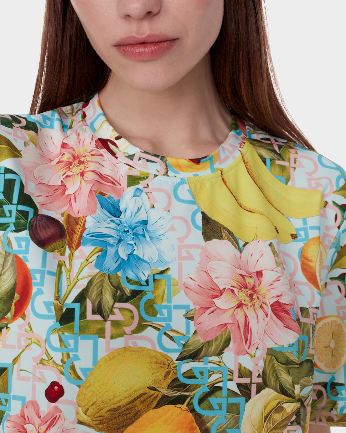 A woman wears the RAYA - 9523004 COCKTAIL RUDSAK F by Rudsak, a colorful neoprene T-shirt featuring a lively fruit cocktail print and geometric shapes on white; only her lower face and upper torso are visible.