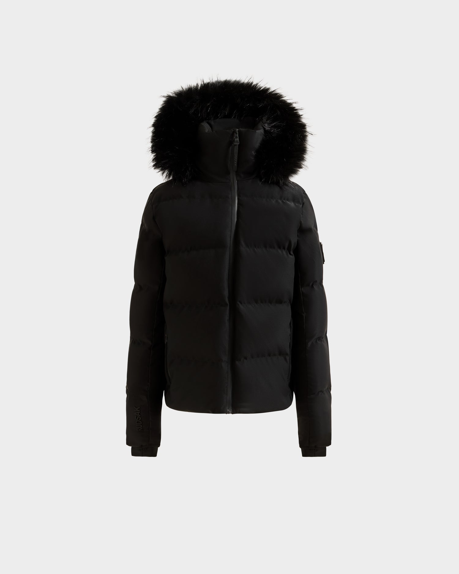 The Rudsak RAEGAN - 0125503 Black is a black puffer jacket with a zip-up front and black faux fur-trimmed hood, shown on a plain light gray background.