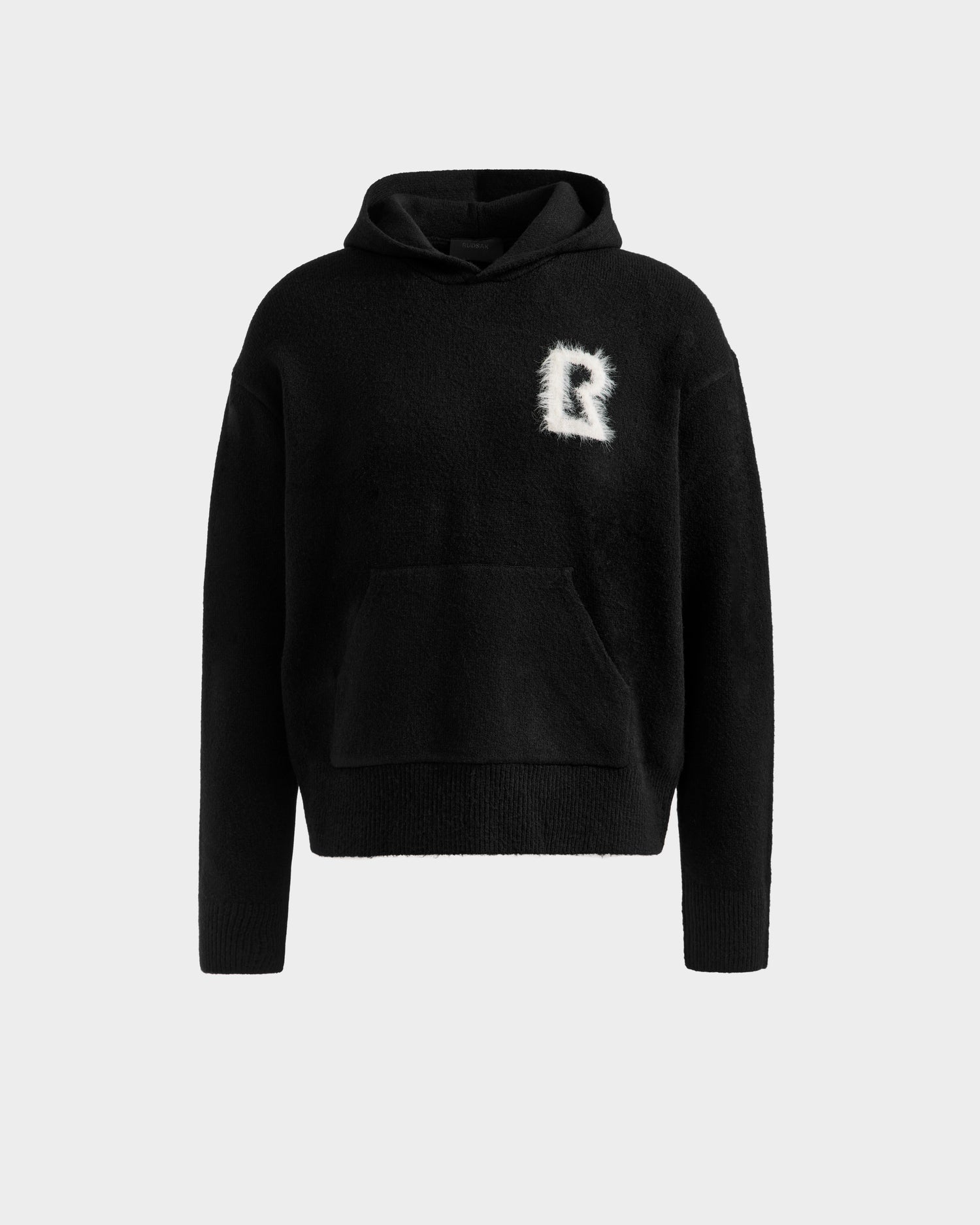 The RAPHAEL - 6525643 Black hoodie by Rudsak features a front pocket and a white fuzzy "R" patch on the left chest, shown on a plain light gray background.
