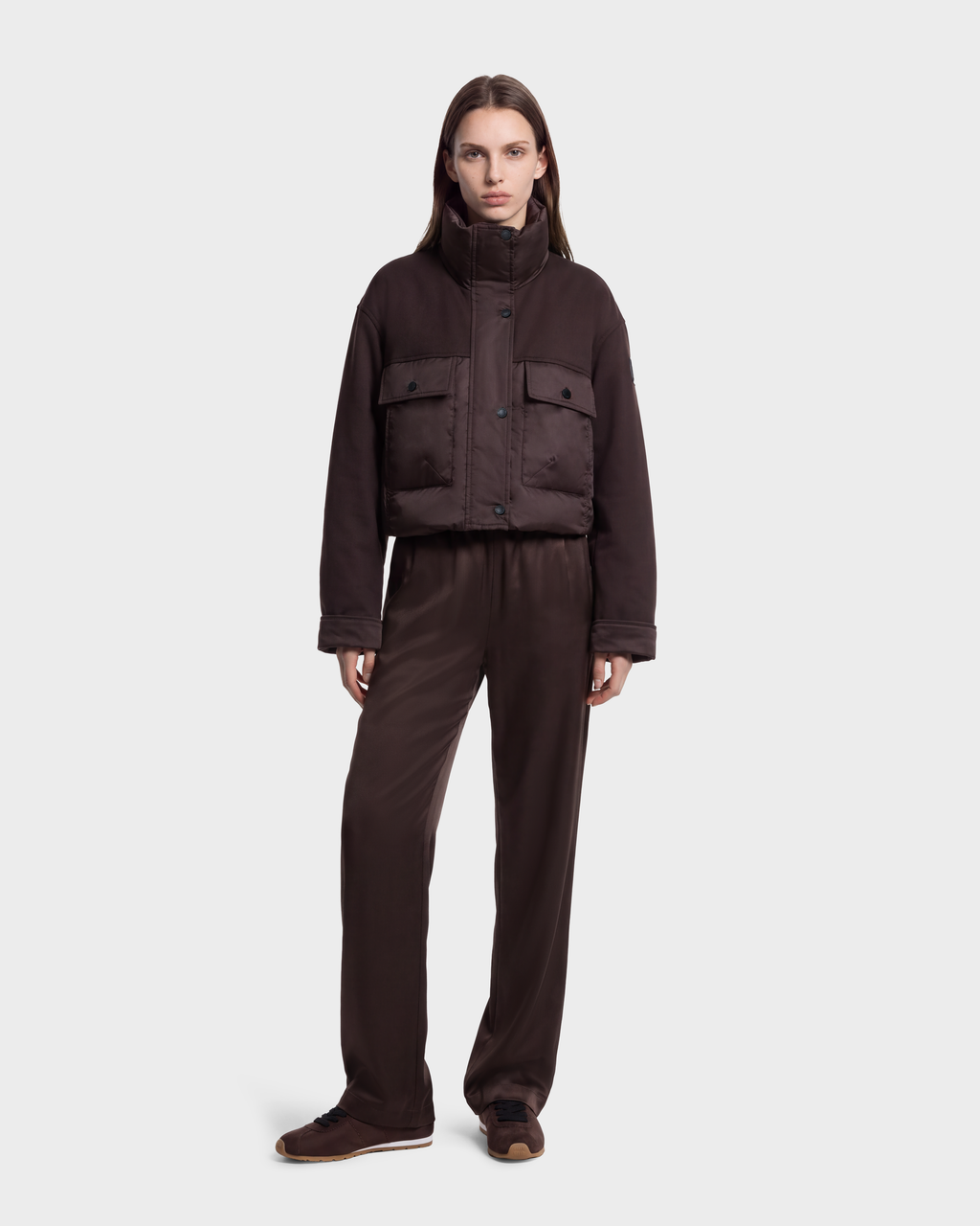 A person wears a dark brown ROME - 8126028 Espresso cropped quilted down jacket with patch pockets over matching trousers and sneakers.
