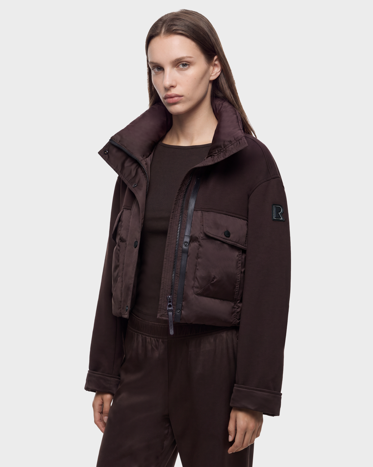 A person wearing a dark brown ROME - 8126028 Espresso cropped, quilted down jacket with a high collar and two chest pockets.