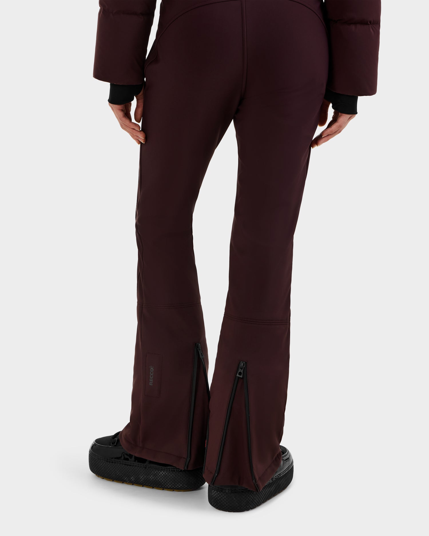 A person wears Rudsak's DINARA - 8125600 Bordeaux dark maroon flared pants with back-calf zippers and black shoes, styled like a women's ski suit, shown waist down against a plain light background.