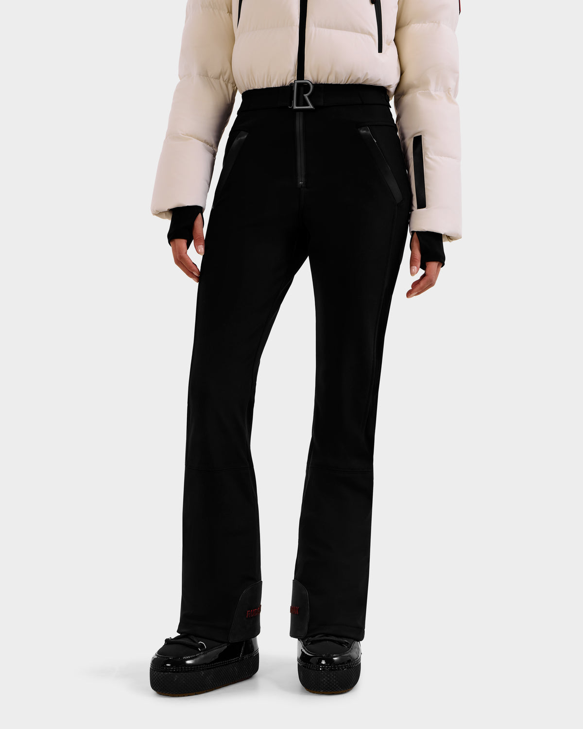 A person wearing Rudsak's DINARA - 8125600 Vanilla white puffer jacket with zippered pockets and RECCO rescue tech, paired with black ski pants and boots, shown from shoulders to feet against a plain background.