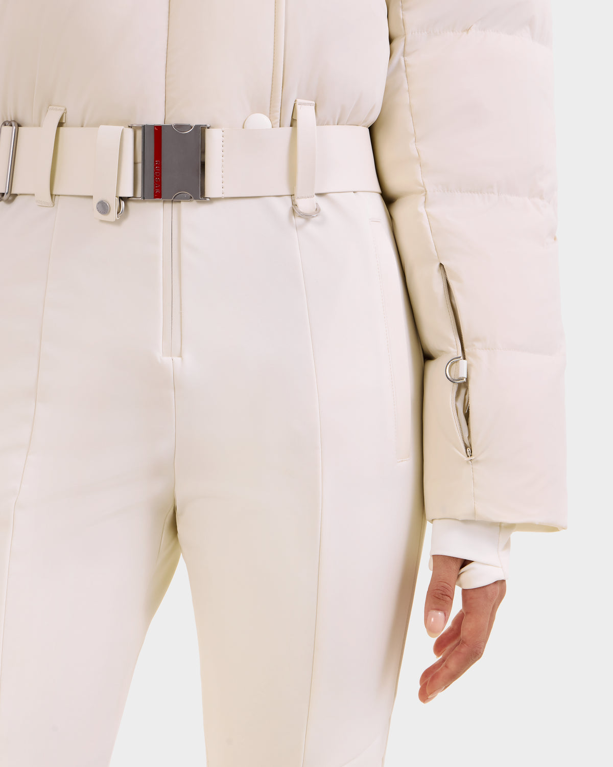 Wearing Rudsak's LOVE - 8124724 Vanilla ski suit, a person stands with one hand by their side—this stylish women's outfit is perfect for alpine adventures.