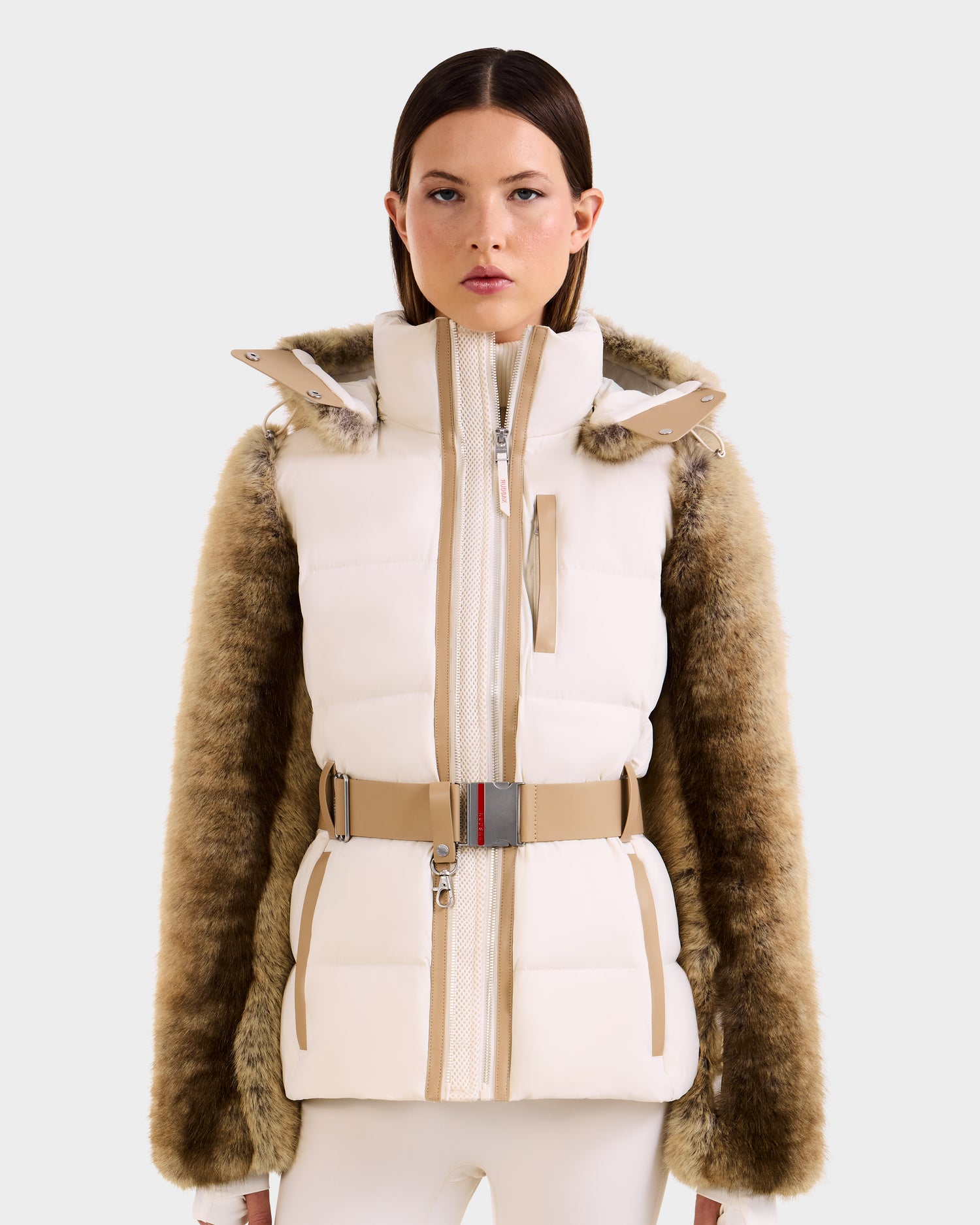 A woman models the Rudsak JOANNA F - 8125593 Mocha—a chic off-white puffer vest with a high collar, beige belt, and faux fur brown sleeves—posing in front of a plain light background.