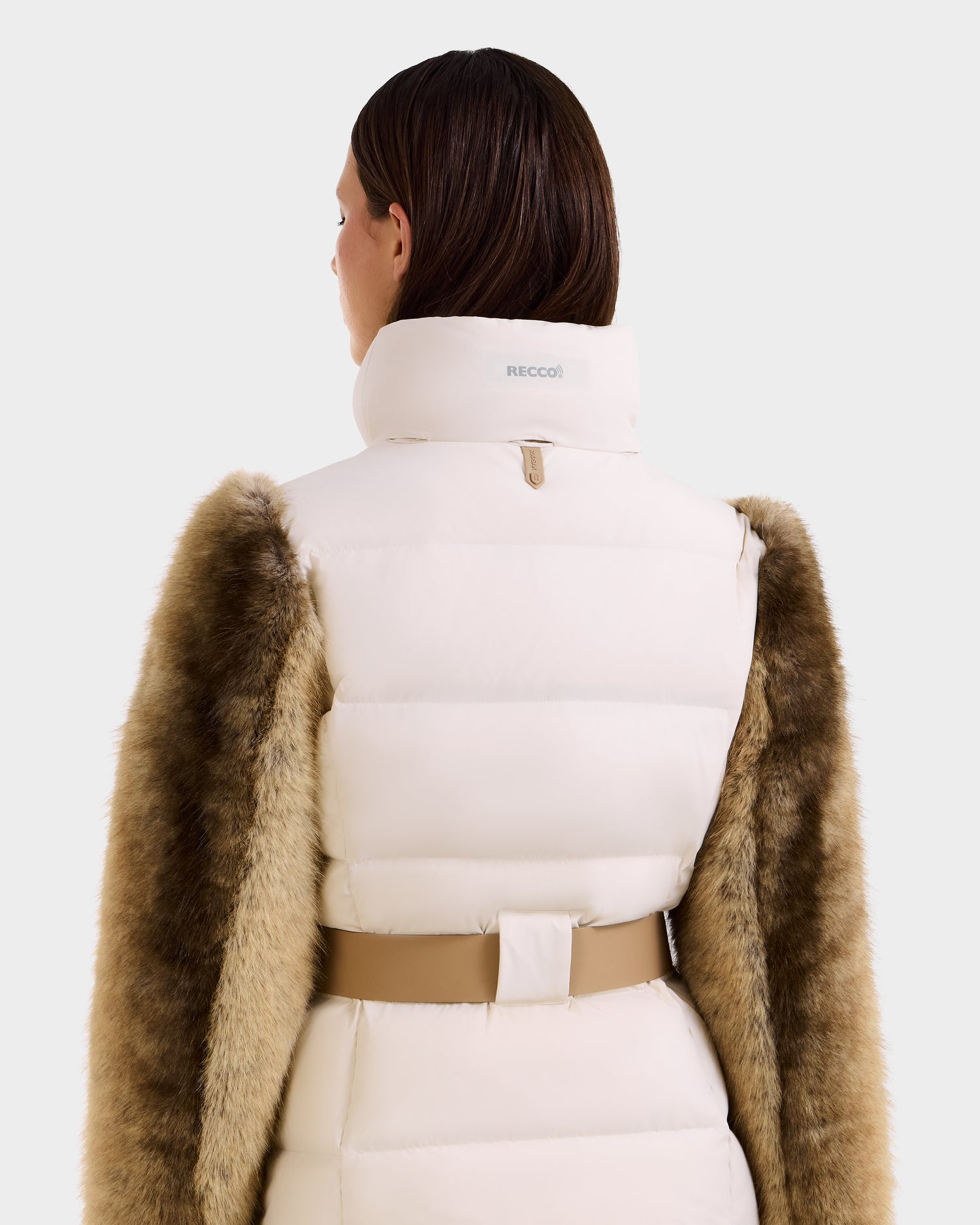 A woman with straight brown hair is seen from the back wearing the Rudsak JOANNA F - 8125593 Mocha down ski jacket, featuring a tan belt and faux-fur-trimmed sleeves, against a plain light background.