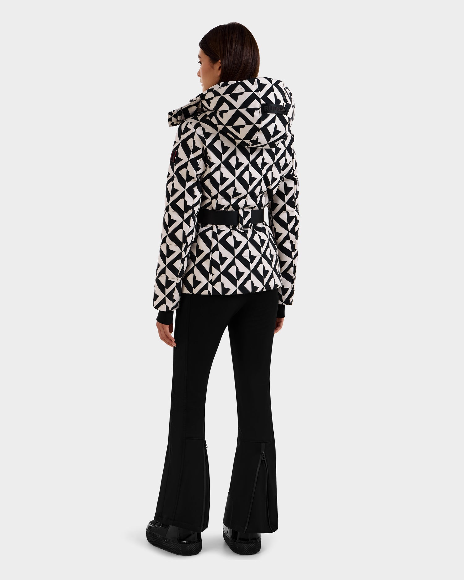 A woman wears the Rudsak JOANNA P - 8125623 Vanilla Monogram, a black and white women’s down ski jacket with a removable hood and RECCO® rescue technology.