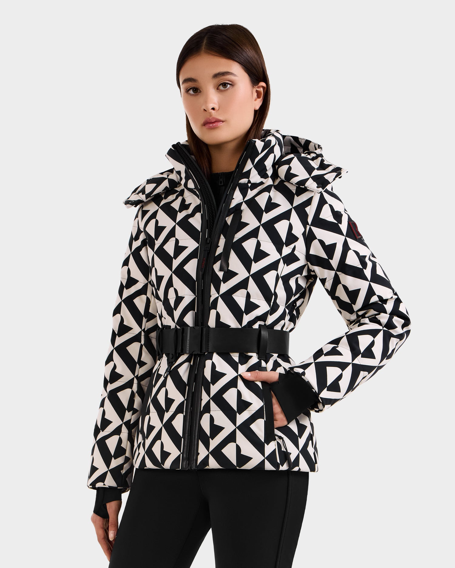 A woman poses with one hand on her hip, wearing the Rudsak JOANNA P - 8125623 Vanilla Monogram women’s down ski jacket against a plain background.