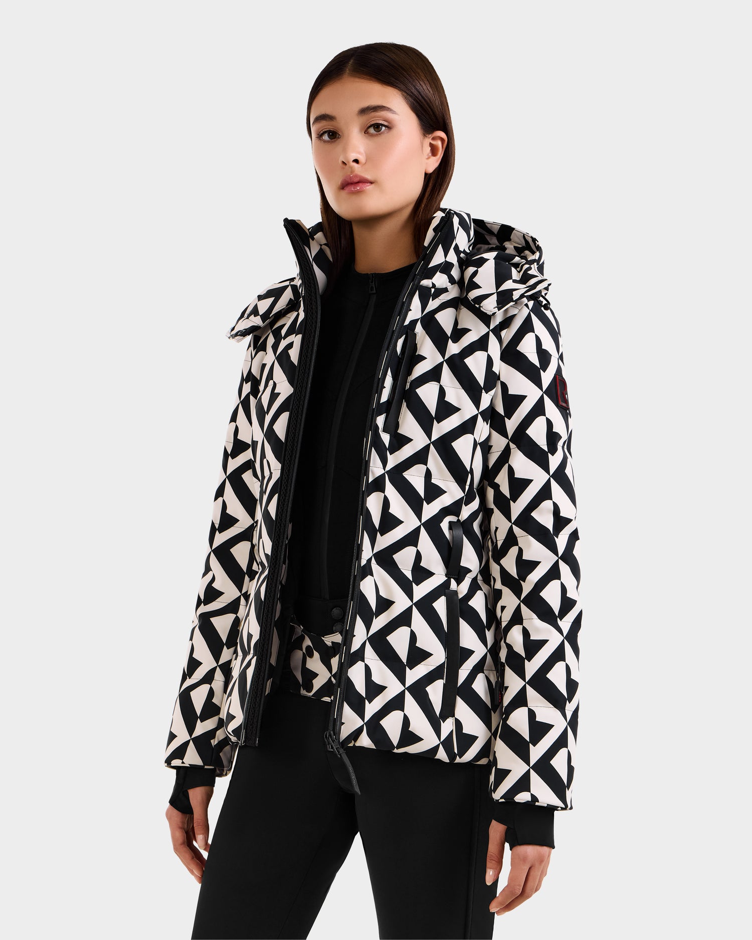 A woman wearing the Rudsak JOANNA P - 8125623 Vanilla Monogram down ski jacket with a removable hood stands against a plain light gray background, looking confidently at the camera.