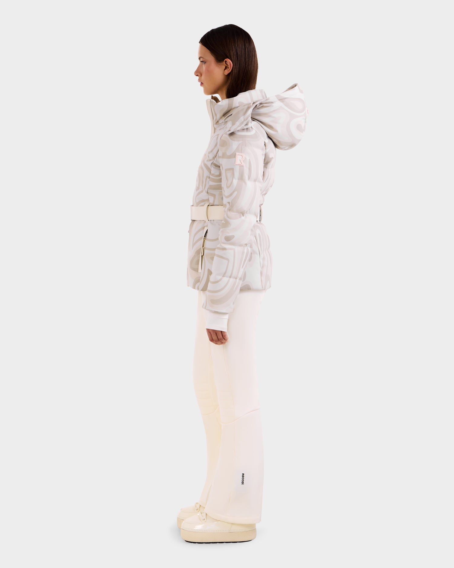 A woman is seen in profile wearing Rudsak's JOANNA P - 8125623 Vanilla Deja vu women’s ski jacket with removable hood, cream flared pants, and matching platform shoes against a plain light gray background.