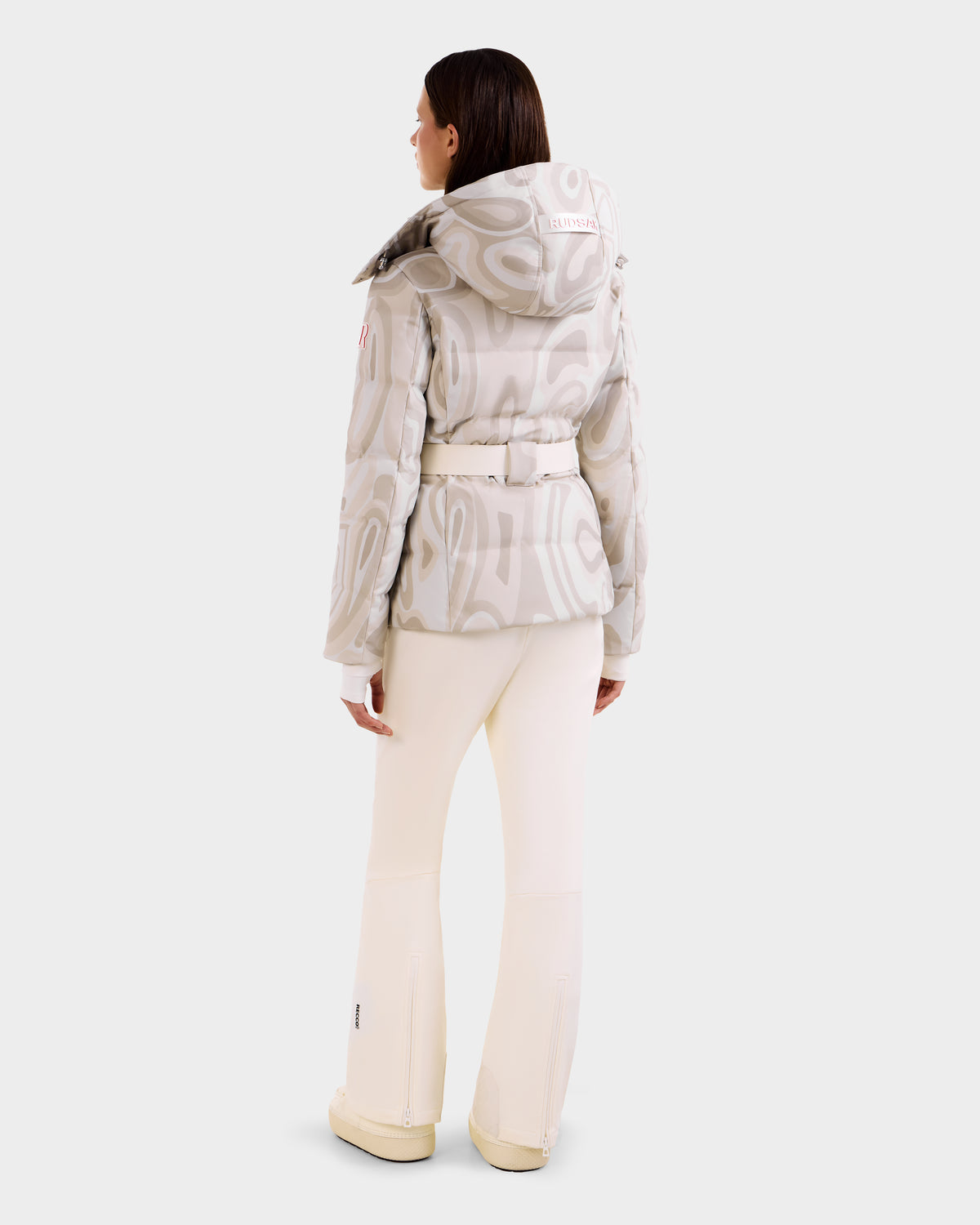 A woman faces away, wearing the Rudsak JOANNA P - 8125623 Vanilla Deja vu down ski jacket with a removable hood, paired with matching cream pants and shoes, set against a plain white background.