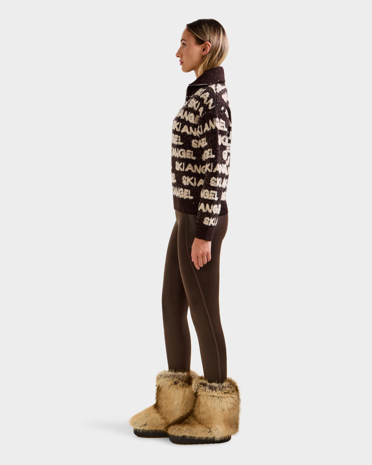 A woman in profile wears the Rudsak LYDIA - 8525687 Espresso patterned alpine pullover sweater, paired with dark brown leggings and tan faux fur boots, set against a plain white background.