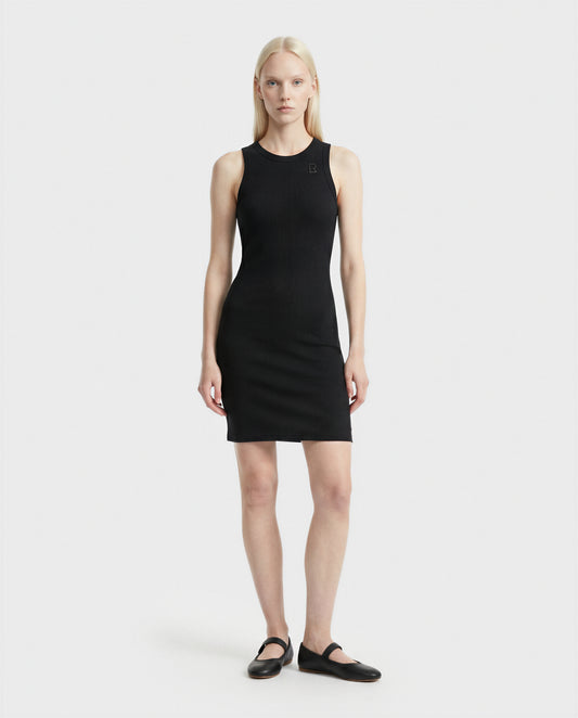 A woman with straight, light blonde hair stands against a white background, wearing the Rudsak ADELLA - L524005 Black sleeveless fitted dress and black flat shoes, facing forward with a neutral expression and arms at her sides.