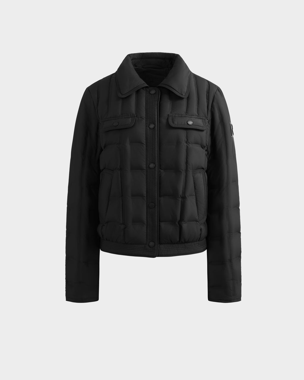 The Rudsak SEOUL - 8126027 Black is a black quilted down-fill shirt jacket with a collar, flap chest pockets, long sleeves, and straight hem for lightweight warmth. Shown on a plain light gray background.