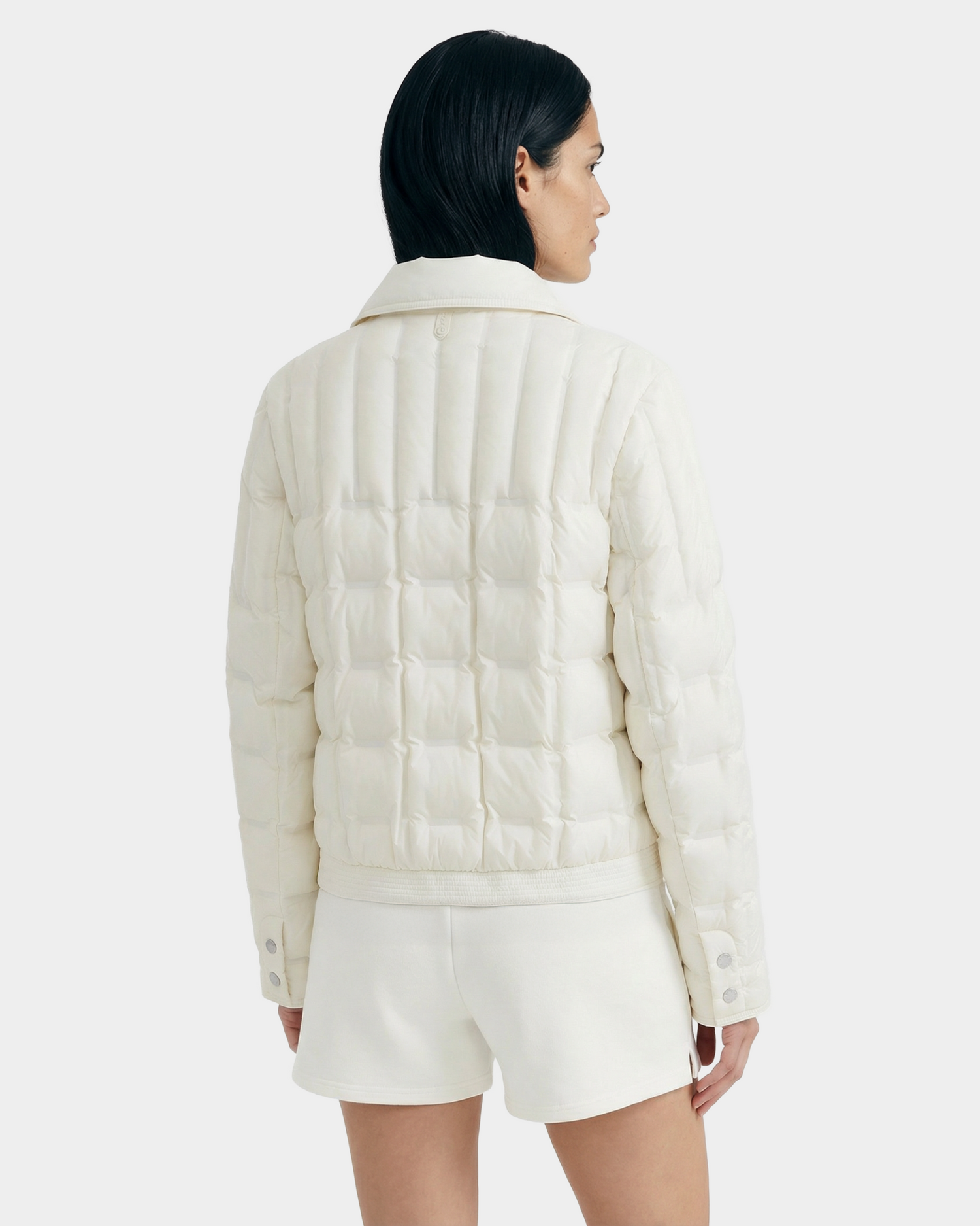 A person with short dark hair, seen from the back, wears Rudsak’s SEOUL - 8126027 Iceland cream-colored, RDS-certified duck down quilted jacket and matching shorts that provide lightweight warmth against a plain light background.