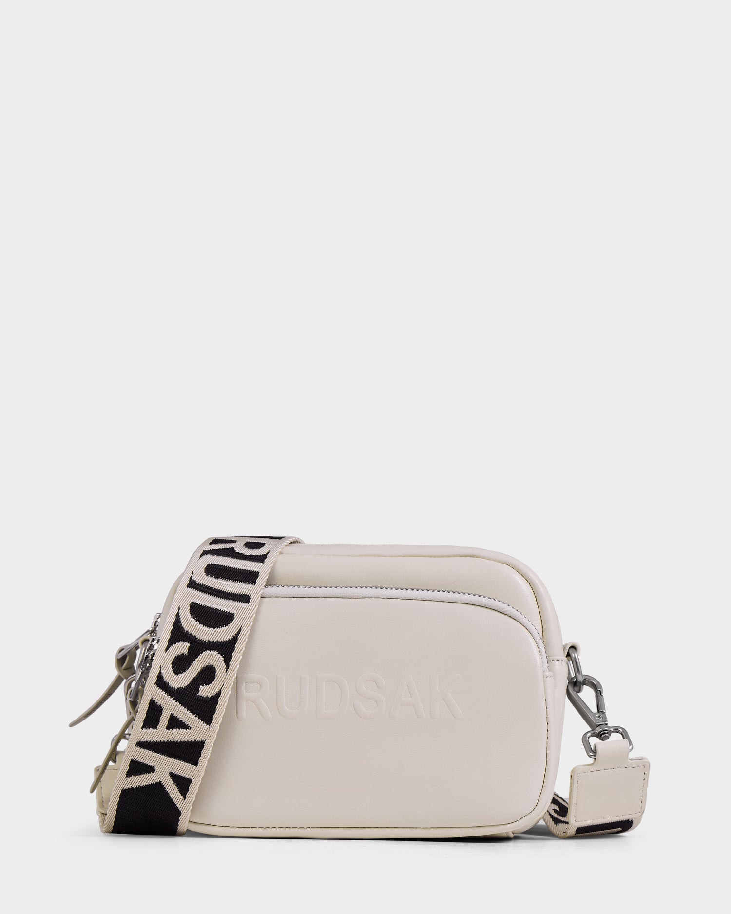 The ZOYA L - 8325543 Vanilla by Rudsak is a small, rectangular cream leather crossbody bag with a bold black-and-white "RUDSAK" strap, front zip pocket, and embossed logo for added style.