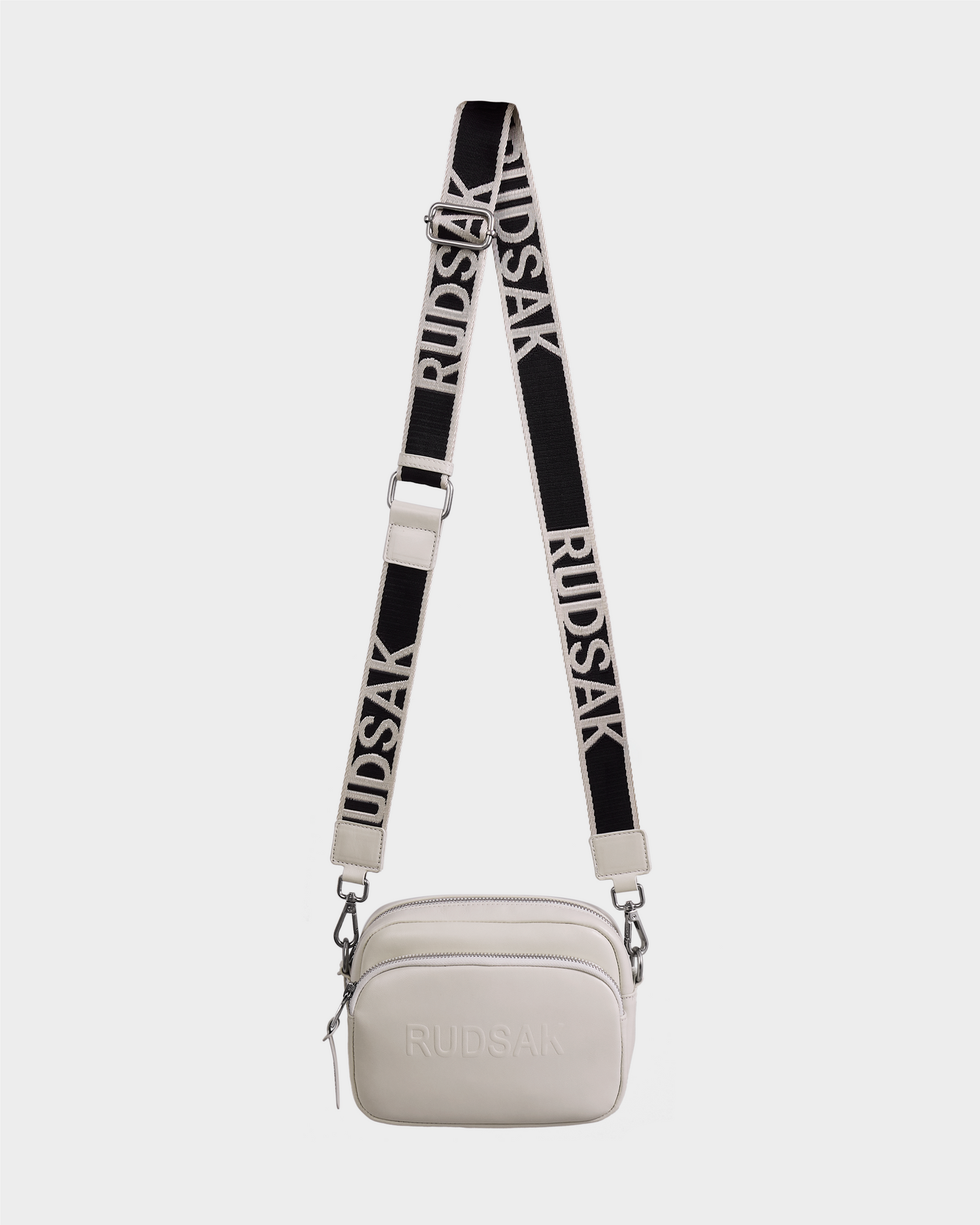 The ZOYA L - 8325543 Vanilla by Rudsak is a small white leather crossbody bag with an adjustable black and white strap featuring “RUDSAK” in bold lettering and the brand name embossed on the front.