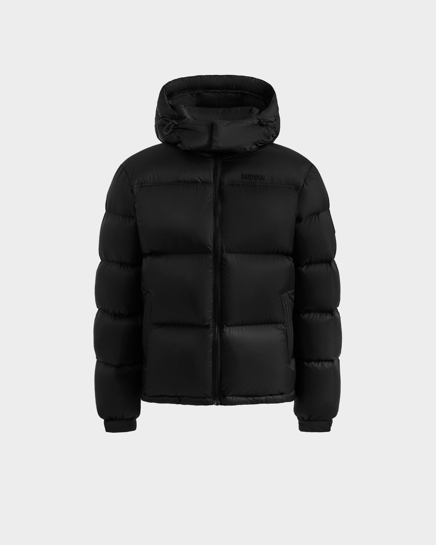 The Rudsak STEFANO - 6125574 Black men’s quilted down puffer jacket features a hood, front zipper, and insulated sections. Displayed on a light gray background, it’s ideal winter outerwear with RDS-certified down for superior warmth.