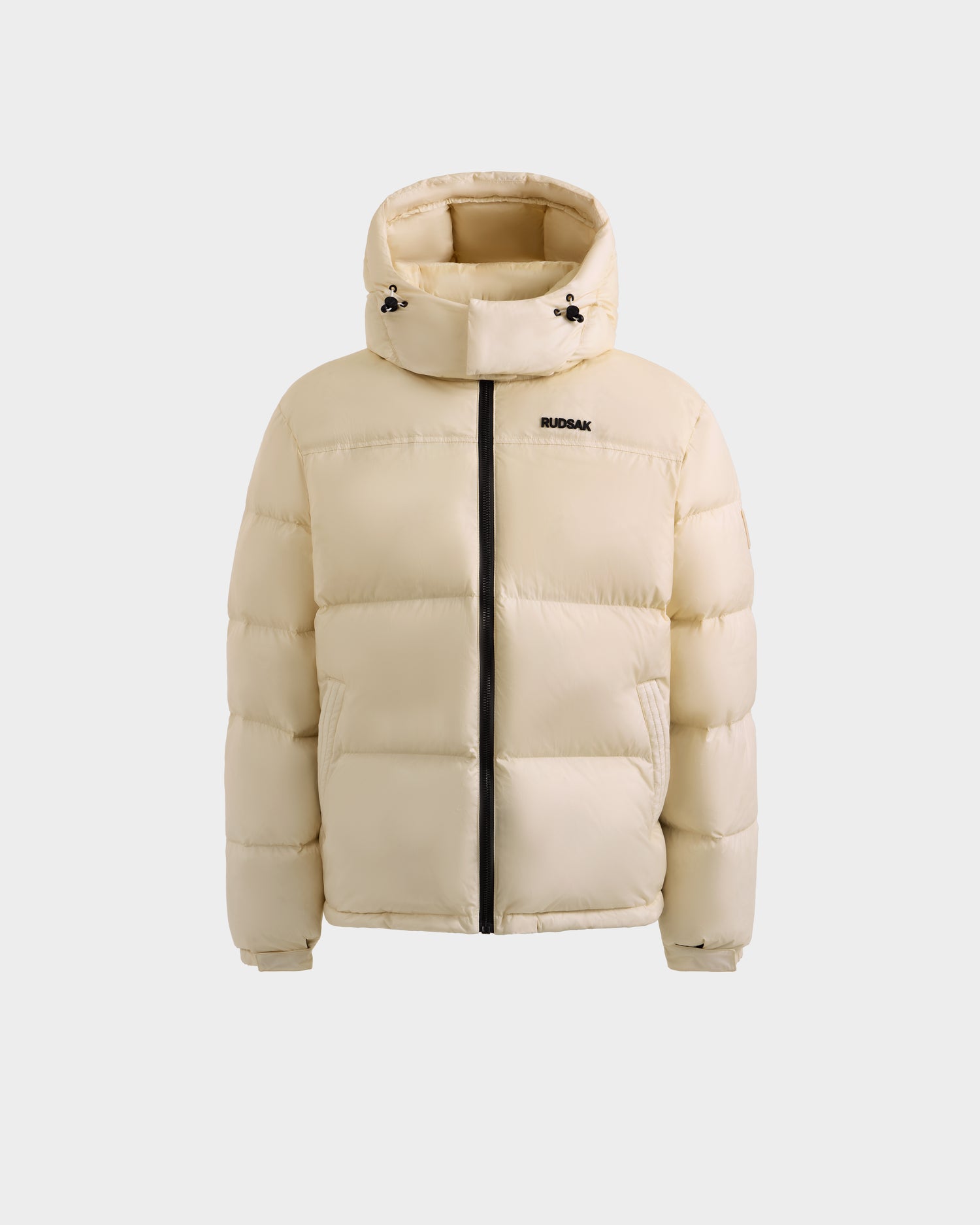 The Rudsak STEFANO - 6125574 Vanilla is a beige men’s quilted down puffer with a hood, black zipper, and small RUDSAK logo on the left chest, shown against a white background as quality winter outerwear.