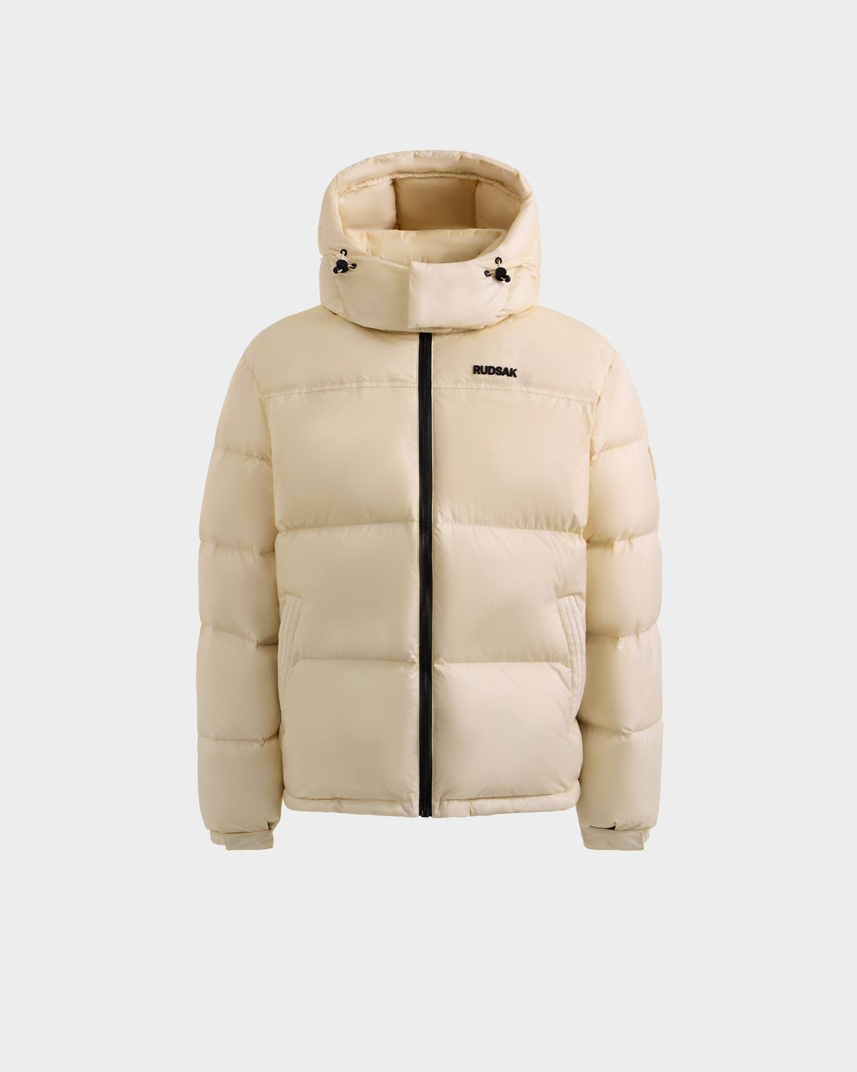 The Rudsak STEFANO - 6125574 Vanilla is a beige men’s quilted down puffer with a hood, black zipper, and small RUDSAK logo on the left chest, shown against a white background as quality winter outerwear.