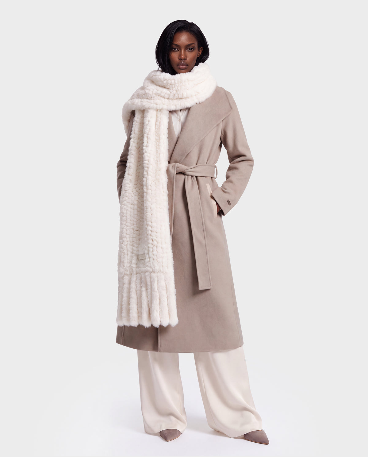 A model wears a TAVIA - 8426511 Vanilla belted beige trench coat over cream-colored wide-leg trousers, styled with a luxurious cold-weather white knit scarf.