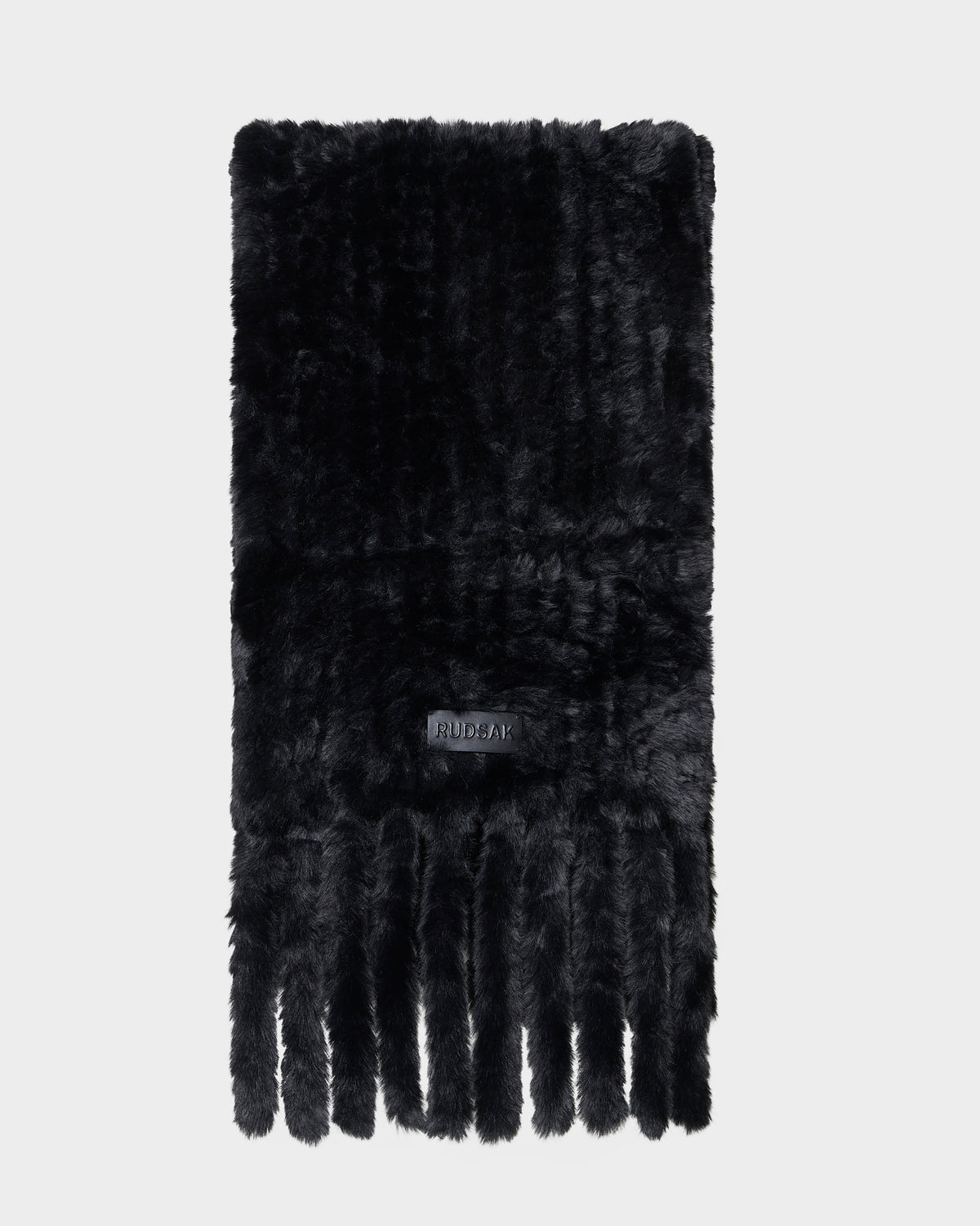 The TAVIA - 8426511 Black scarf by Rudsak is a black faux fur accessory with a soft texture, adorned with a label and multiple long fringes at the ends, displayed on a plain white background.