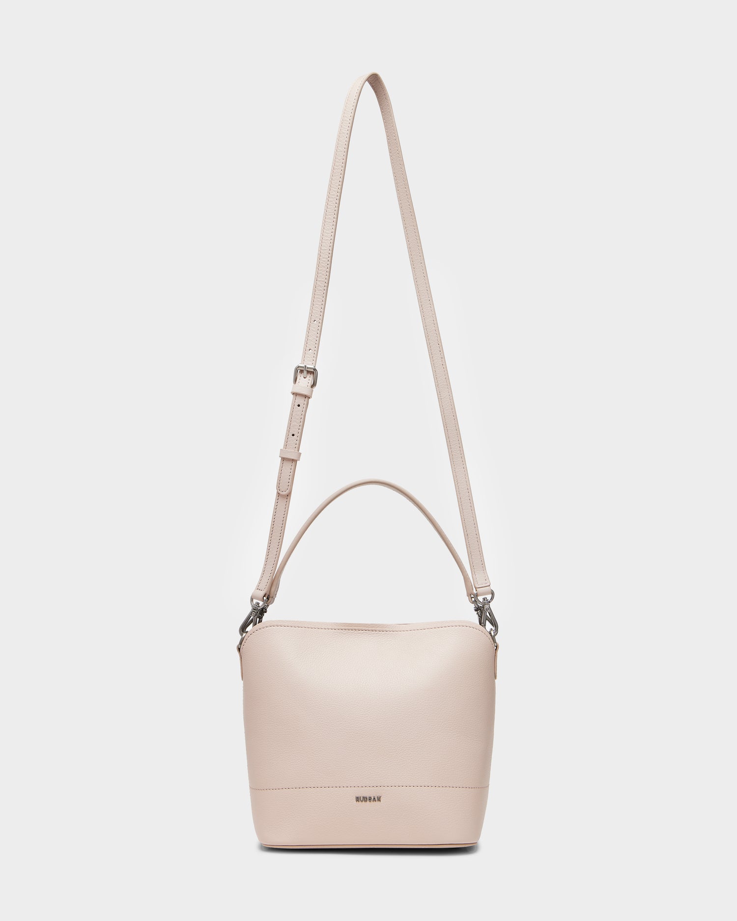 The Rudsak ANIA SM - 8325009 is a soft pink women’s pebble leather hobo bag with an adjustable crossbody strap, short handle, minimalist design, and a small metal logo at the bottom center.