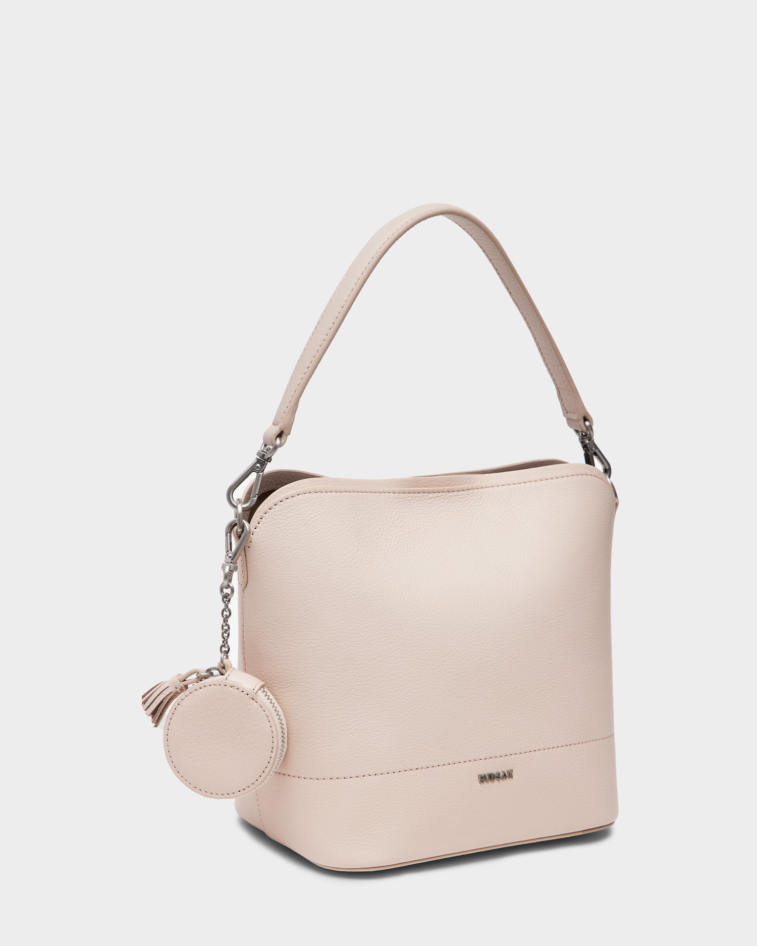 The Rudsak ANIA SM - 8325009 is a soft pink women’s pebble leather hobo bag with a short handle, silver hardware, a round coin pouch with tassel, subtle front logo, and an adjustable crossbody strap for versatile carrying.