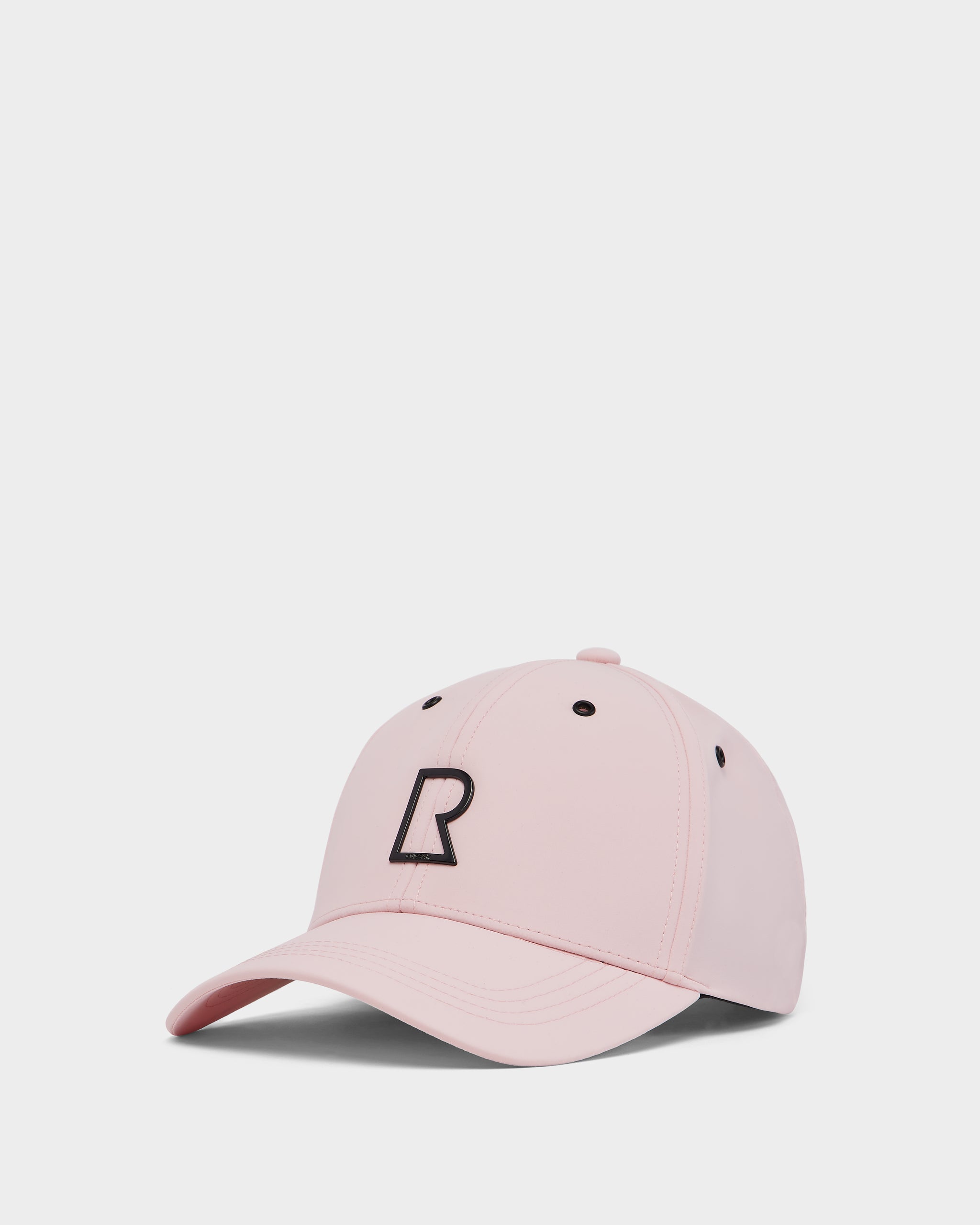 The Rudsak ARSENE - 9422504 Light Pink unisex baseball cap features a light pink design with a black stylized R and black ventilation eyelets, and is shown against a plain white background.