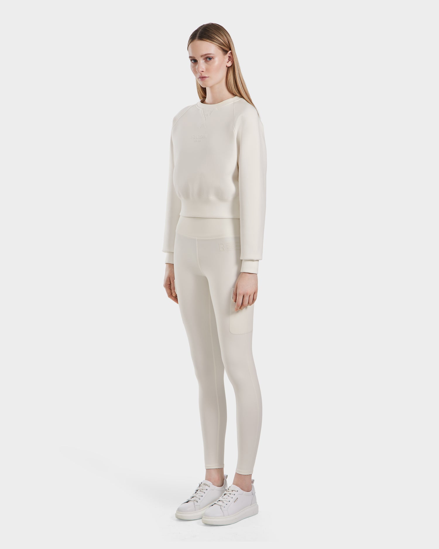 A woman faces slightly to the side, wearing the Rudsak BETSY - 8525087 Iceland crewneck sweater with matching leggings and white sneakers, set against a plain white background.