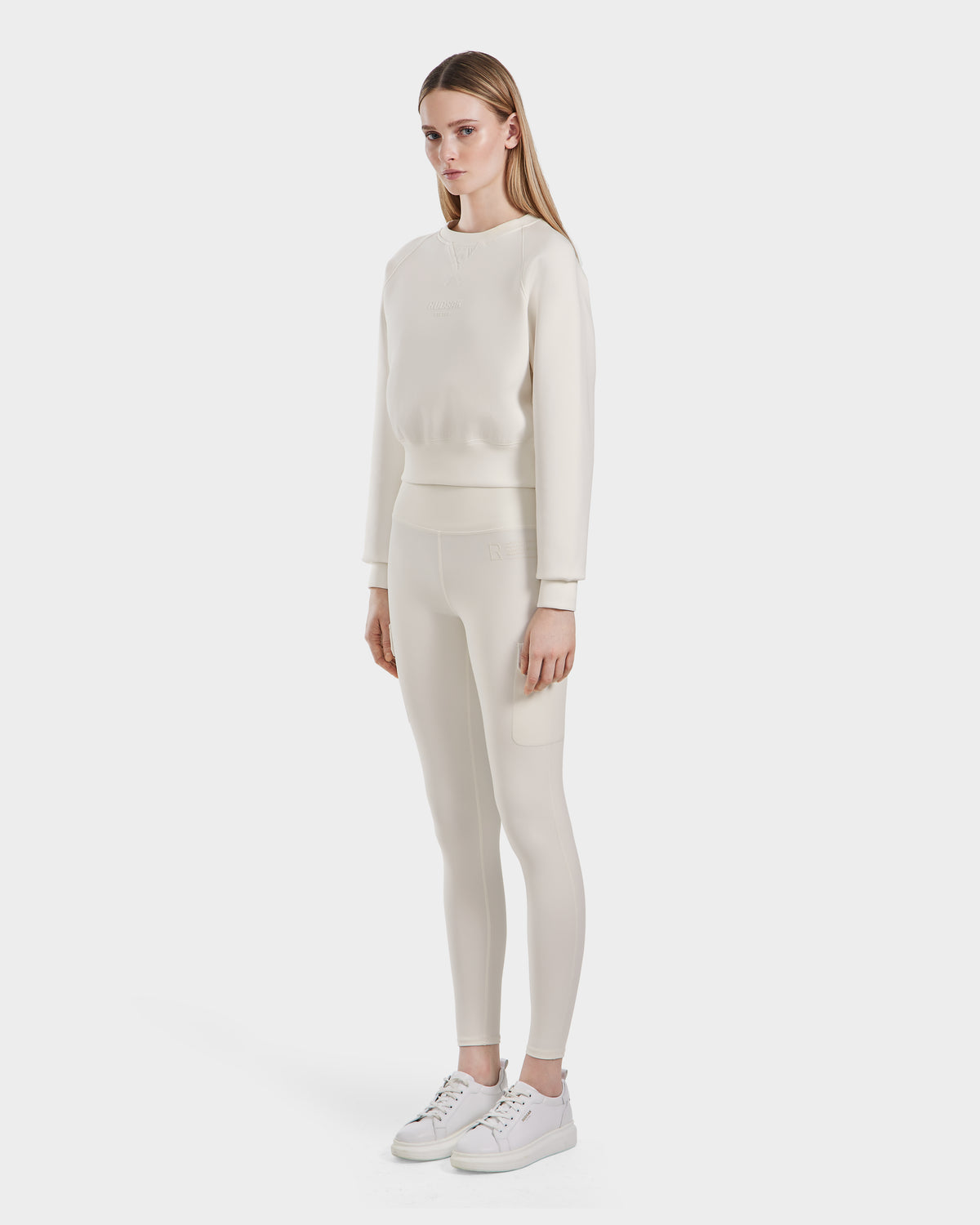 A woman faces slightly to the side, wearing the Rudsak BETSY - 8525087 Iceland crewneck sweater with matching leggings and white sneakers, set against a plain white background.