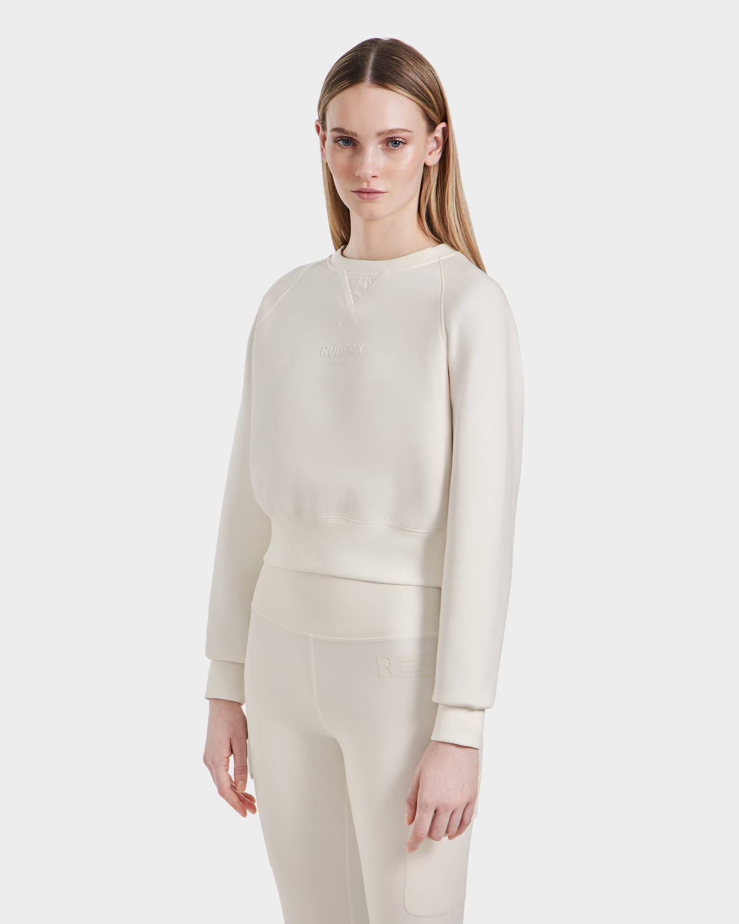 A woman with long, straight, light brown hair wears the off-white BETSY - 8525087 Iceland sweater and matching leggings from Rudsak, standing against a plain white background and looking at the camera with a neutral expression.