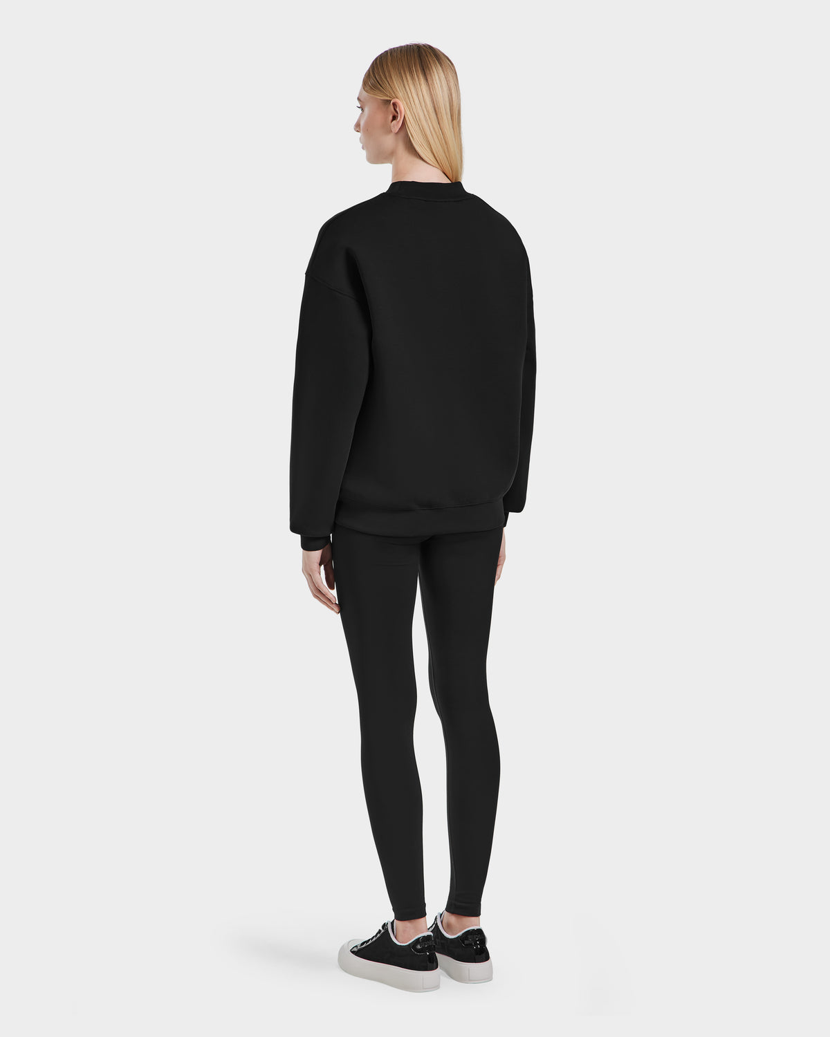 A woman wears the Rudsak BRYN - 9524007 Black W cotton crewneck sweatshirt, highlighting its everyday fit and genderless sizing for effortless style.