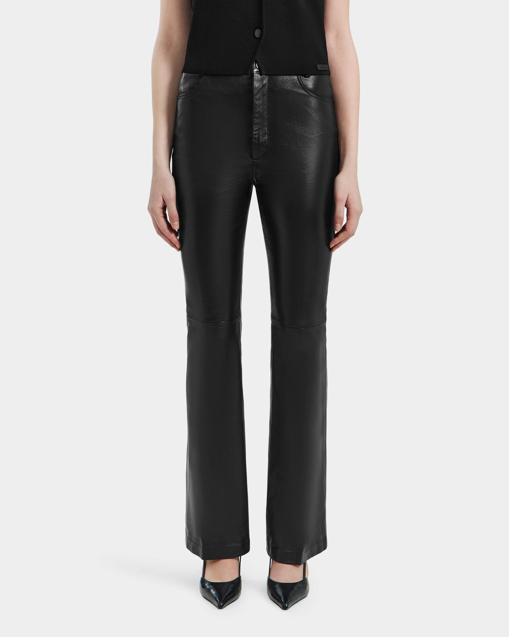 A person stands facing forward in Rudsak’s CARISSA - 8524545 Black leather pants with black pointed-toe heels. Only the lower torso, legs, and arms are shown against a plain white background.