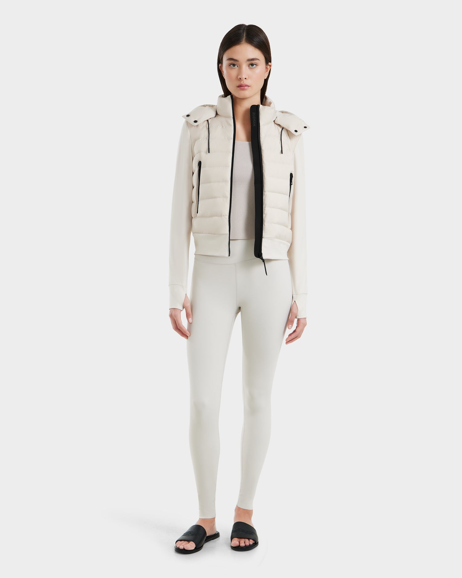 A woman stands facing forward wearing the Rudsak CASSA - 8125057 Vanilla womens transitional jacket, paired with matching leggings, a white top, and black slide sandals against a plain white background.