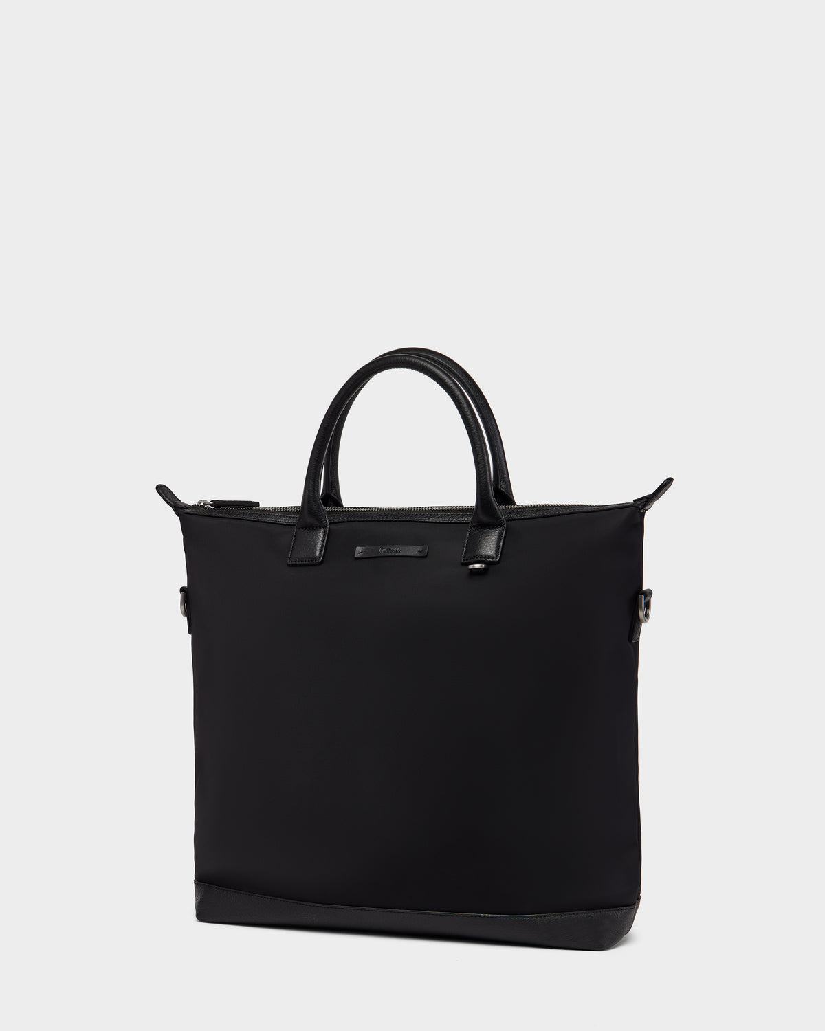 The Rudsak DEXTER - 9324513 Black is a minimalistic black canvas tote bag with two short handles and a zipper closure, showcased against a plain light gray background.
