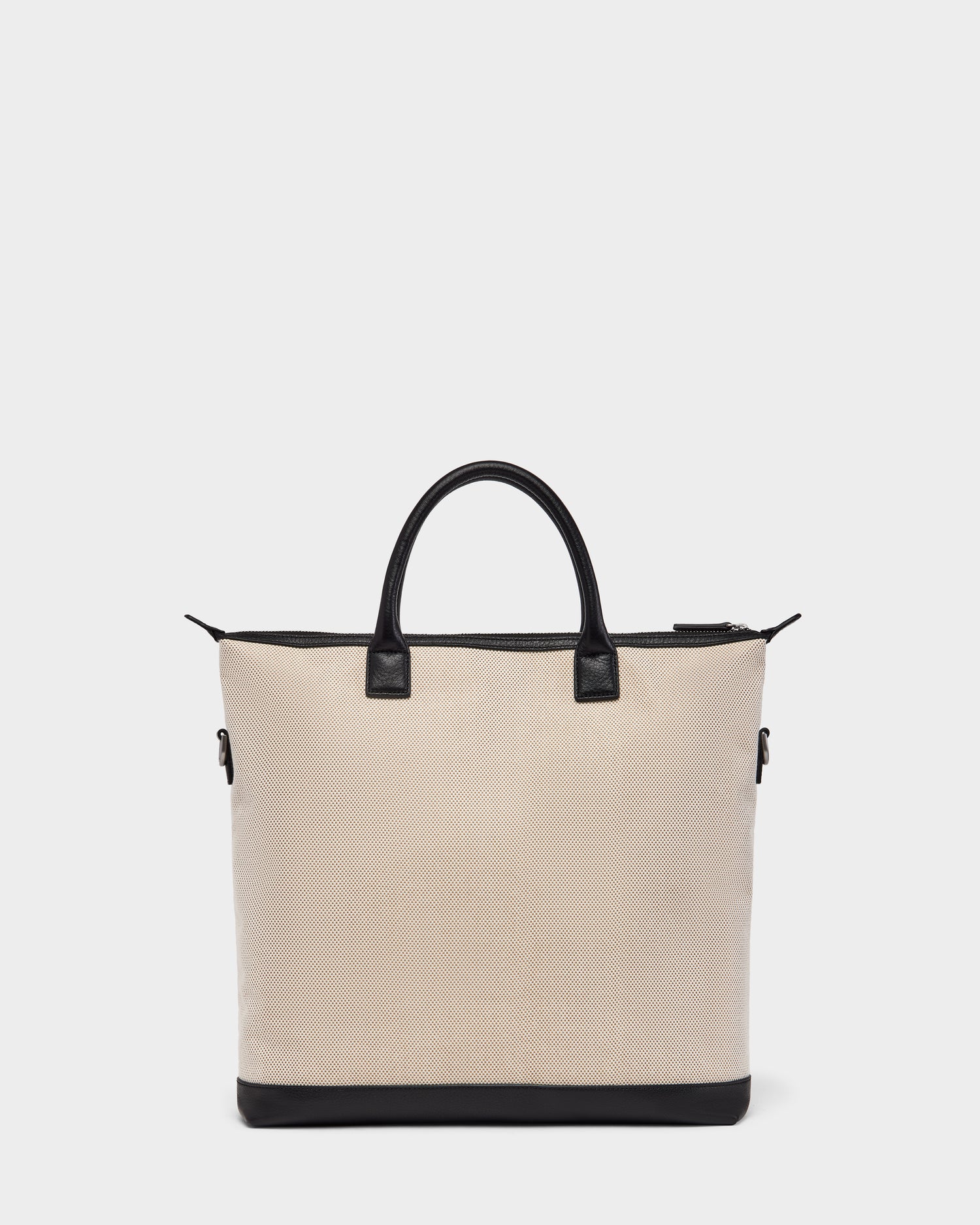 The Rudsak DEXTER - 9324513 Vanilla is a beige canvas tote with black leather handles, trim, and base. Its zippered top and rectangular shape make this unisex bag a versatile accessory for any occasion. Displayed on a plain white background.