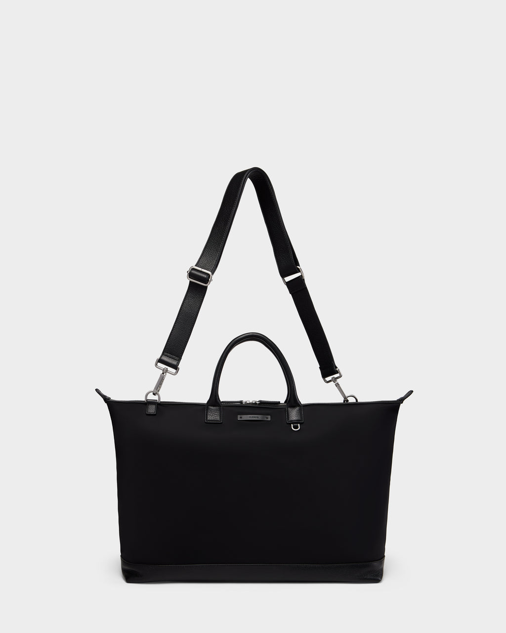 The Rudsak DUBLIN - 9324514 Black is a unisex, rectangular canvas leather bag with short handles, a long adjustable strap, silver hardware, and a minimalist design set against a plain white background.