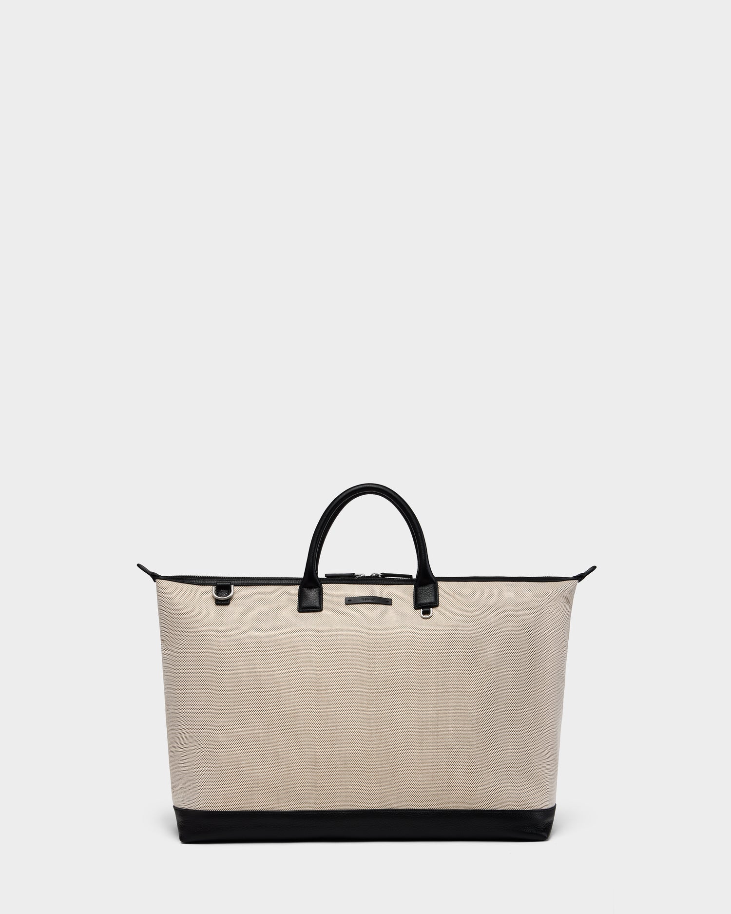 The Rudsak DUBLIN - 9324514 Vanilla is a large beige canvas leather unisex weekender tote with black handles and trim, featuring a structured, minimalist design. It’s showcased on a plain light gray background.