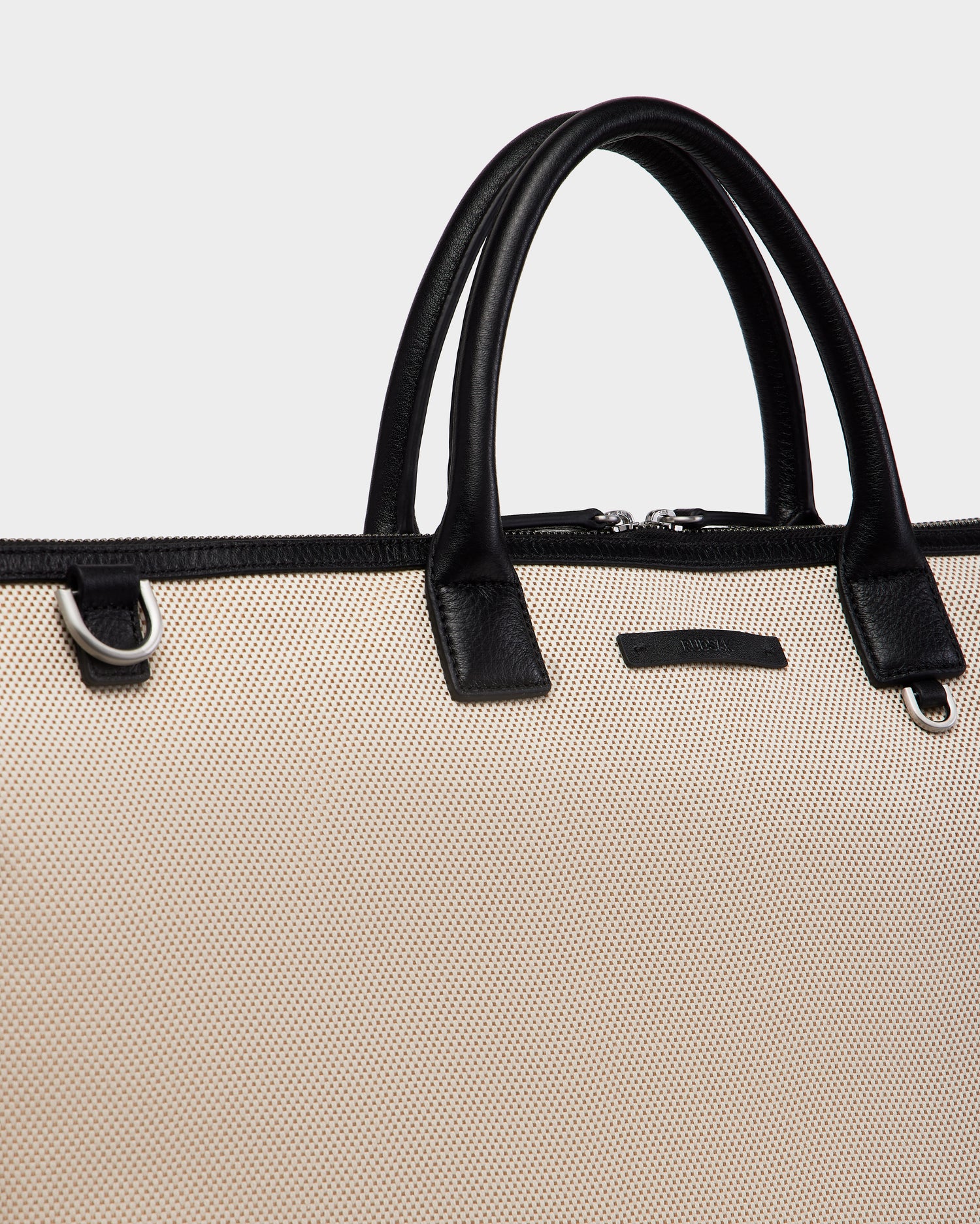 A close-up of the Rudsak DUBLIN - 9324514 Vanilla tote, a beige canvas leather weekender with black handles and silver hardware, set against a plain light gray background.