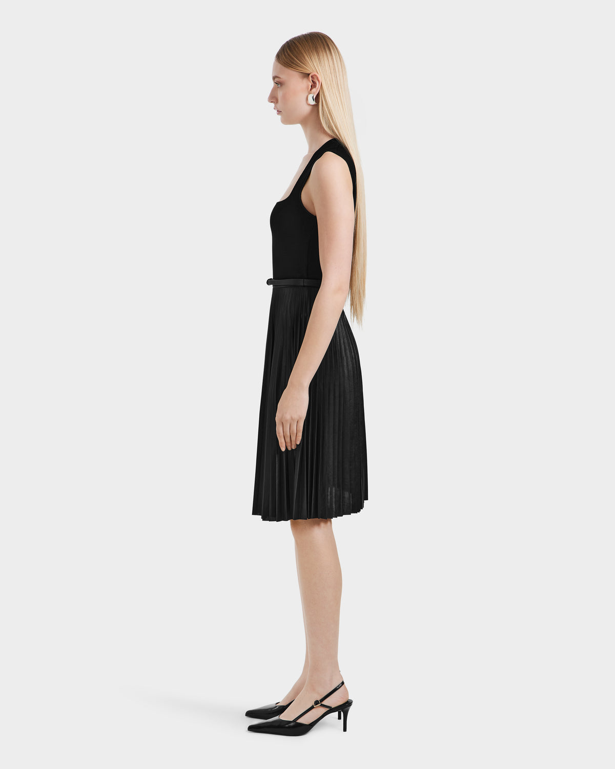 A woman in profile wears the JANE - 8525029 Black pleated midi skirt by Rudsak, paired with black slingback heels and straight hair, set against a plain white background.