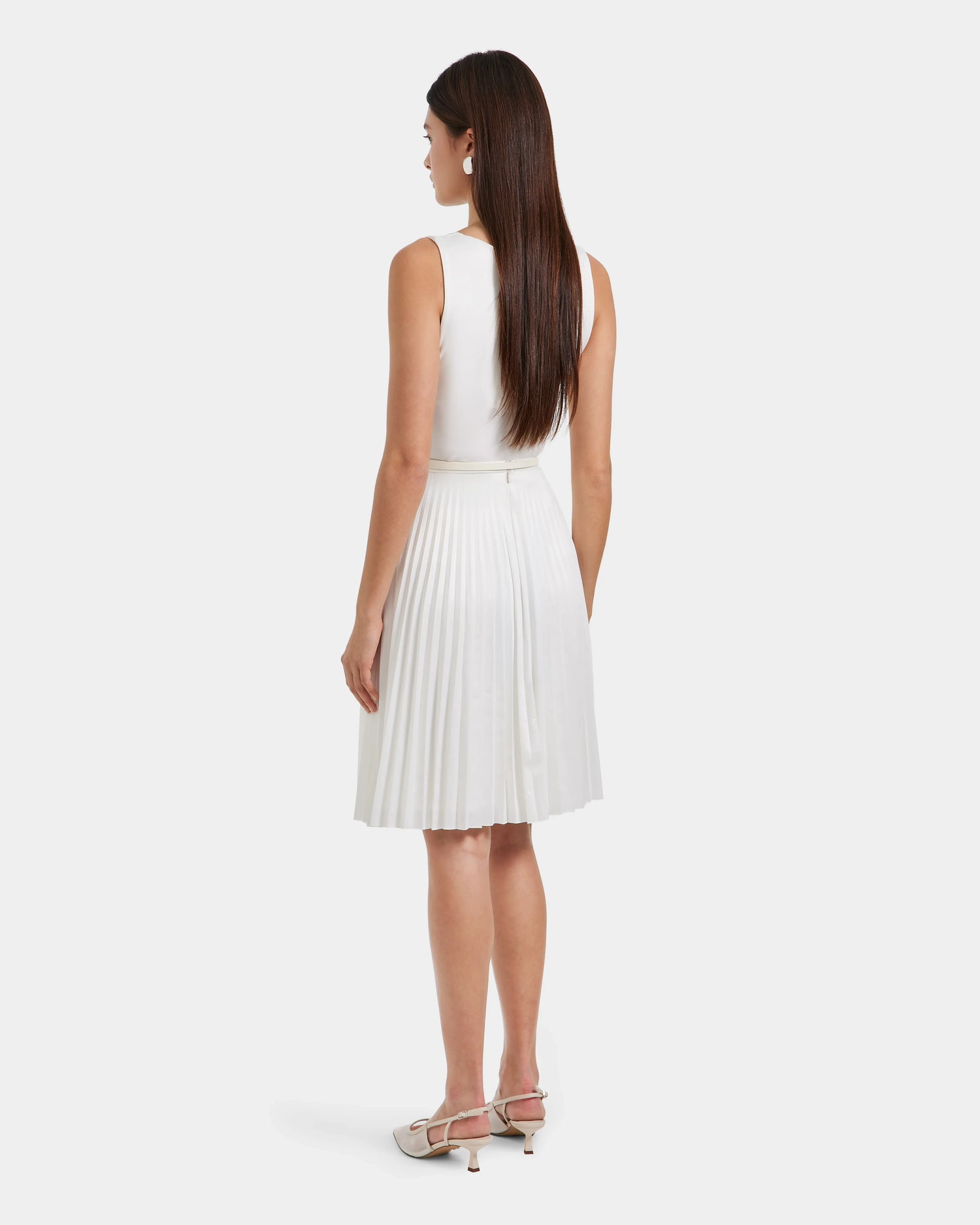 A woman with long, straight brown hair faces away, wearing the sleeveless white JANE - 8525029 Iceland midi pleated dress by Rudsak and white heels. She stands against a plain, light background.
