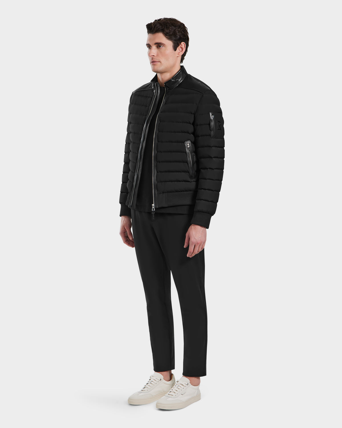 A man wears the Rudsak JOSHUA - 6124542 Black quilted light down jacket with black pants and white sneakers, standing against a plain white background and facing slightly to the side with a neutral expression.