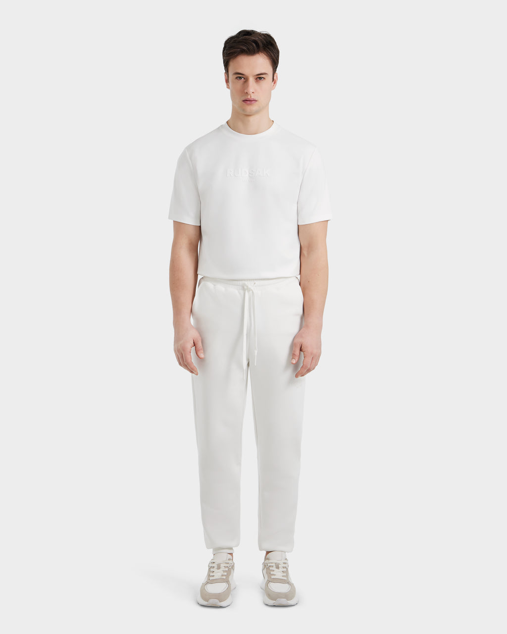 A person stands facing forward, wearing the Rudsak JOSS - 9524009 Iceland M shirt, premium cotton joggers, and light sneakers against a plain white background.