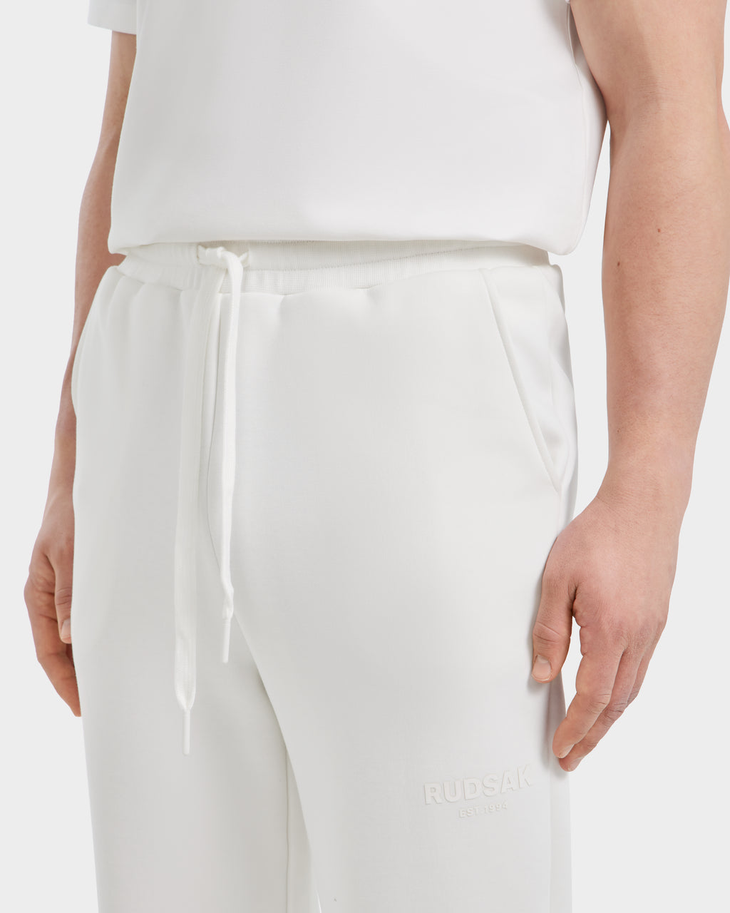 A person wears a white short-sleeve shirt and JOSS - 9524009 Iceland M premium cotton joggers by Rudsak, featuring the brand name embossed near the left pocket for a sleek, modern look.