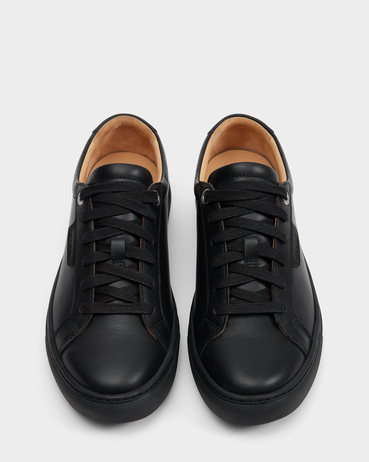 A pair of Rudsak LARIS - 6225000 Black mens leather sneakers with matching black laces, tan interiors, and simple stitching, shown from above on a light gray background.