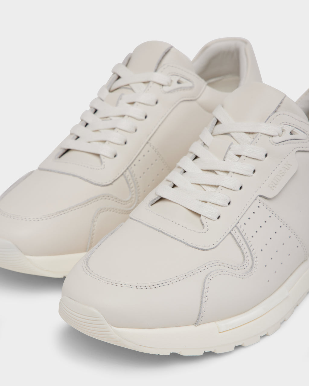 A close-up of Rudsak’s MALONE - 6225010 Iceland men’s off-white leather sneakers features white laces, minimal stitching, a textured rubber sole, and a subtle side logo for a clean, modern look.
