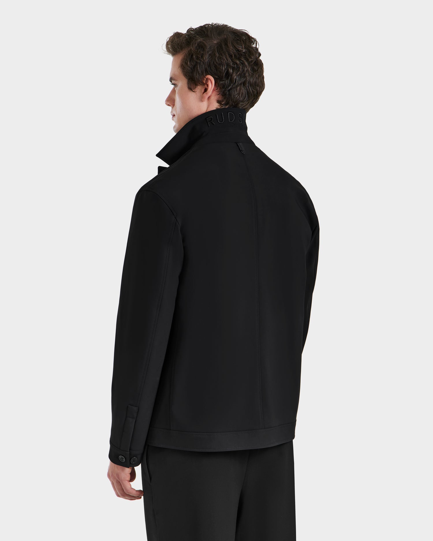 A man wearing the Rudsak MATTHEW - 6125004 Black tailored blazer and pants stands with his back and side to the camera, collar turned up, against a plain light gray background.