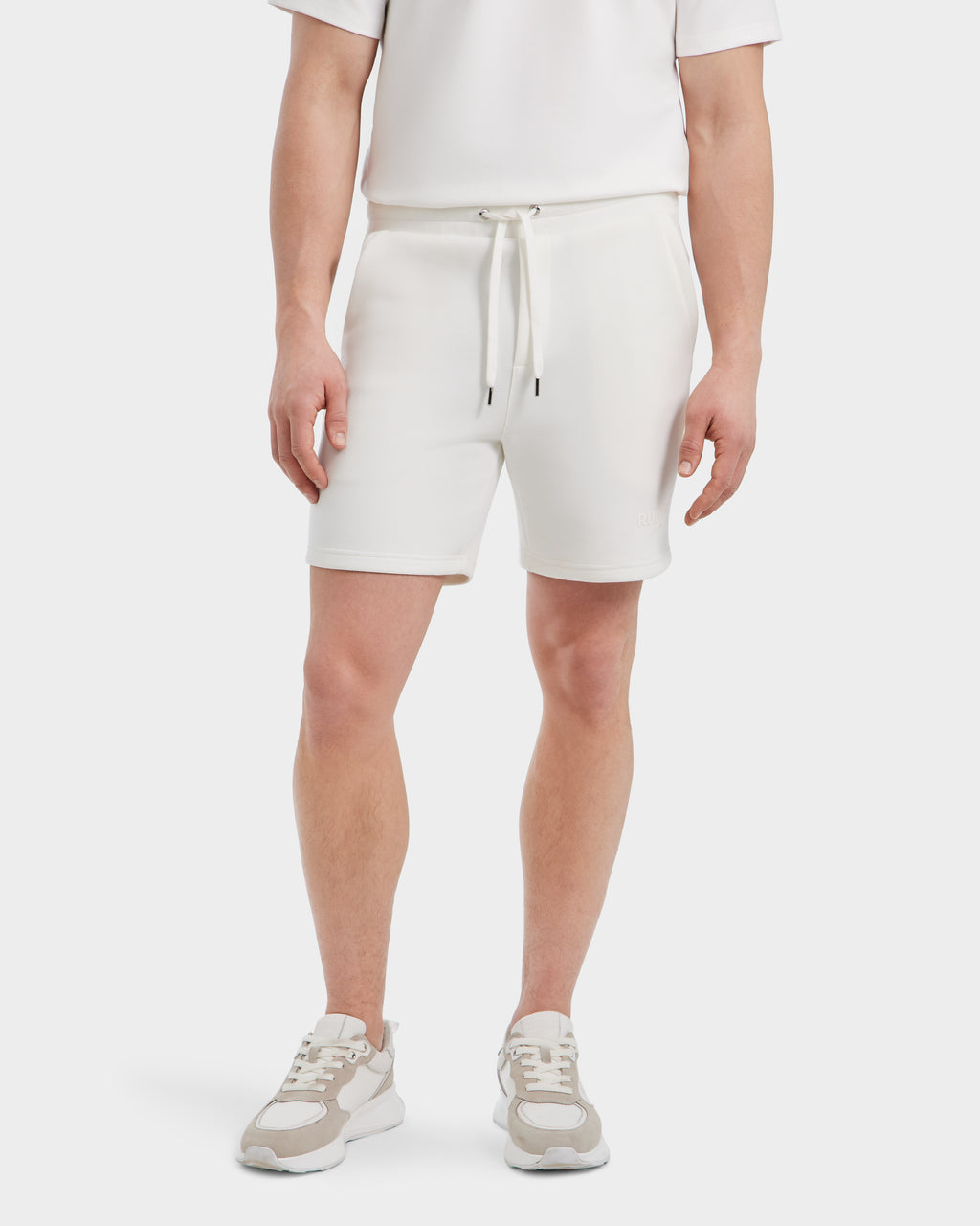 A person wearing the Rudsak PASCAL - 6524022 ICELAND men’s jersey shorts, a white short-sleeve shirt, and beige-and-white sneakers stands against a plain white background.