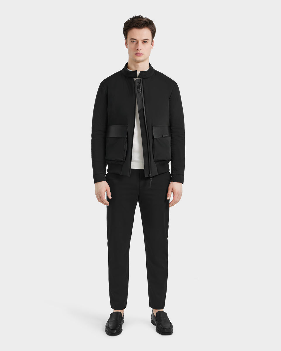 A man faces forward against a plain white background, wearing the Rudsak PETER - 6125001 Black jacket with vegan leather accents, black pants, a white shirt, and black shoes.